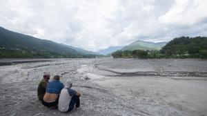 Tres hombres observan cómo el agua fluye por una comunidad afectada por una inundación glacial cerca de la frontera entre Nepal y China que mató a cientos de personas