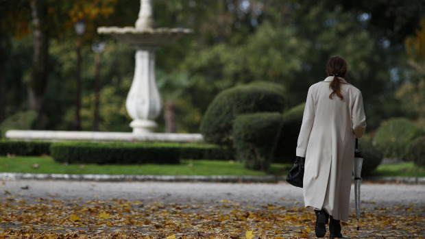 Una mujer camina por el parque Rosalía de Castro de Lugo tapizado de hojas con colores otoñales