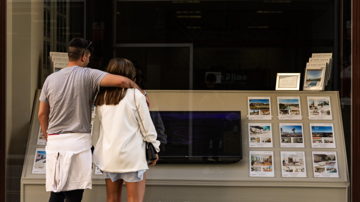 Una pareja consulta los precios de los pisos en el escaparate de una inmobiliaria
