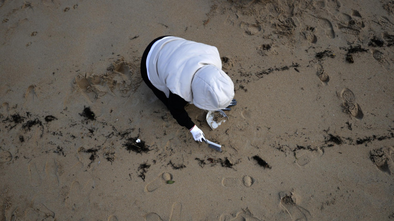 Unha persoa recolle pélets nunha praia galega