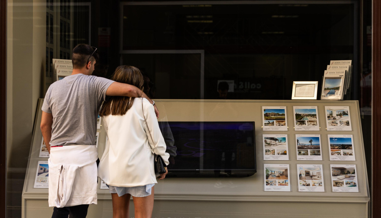 Una pareja consulta los precios de los pisos en el escaparate de una inmobiliaria