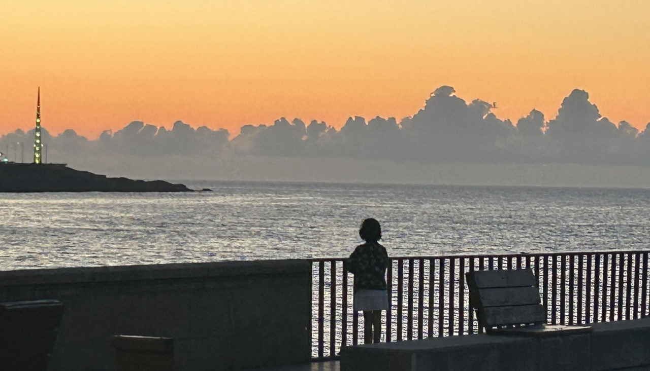 Una niña observa el atardecer en litoral coruñés, desde la Coraza
