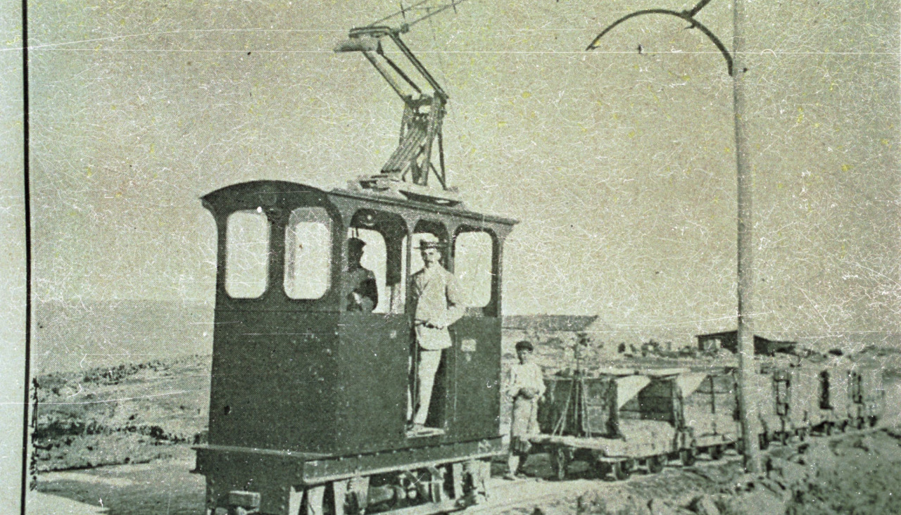 Dos personas sobre el primer ferrocarril eléctrico de Galicia, en A Coruña, con material para construir la dársena del puerto, en 1909