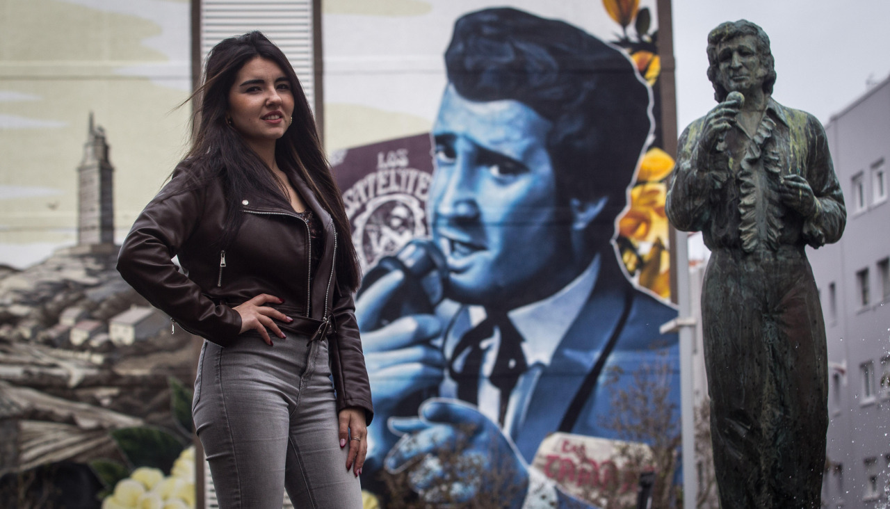 María Lamas posa ante la estatua y el mural dedicado a Pucho Boedo en O Ventorrillo
