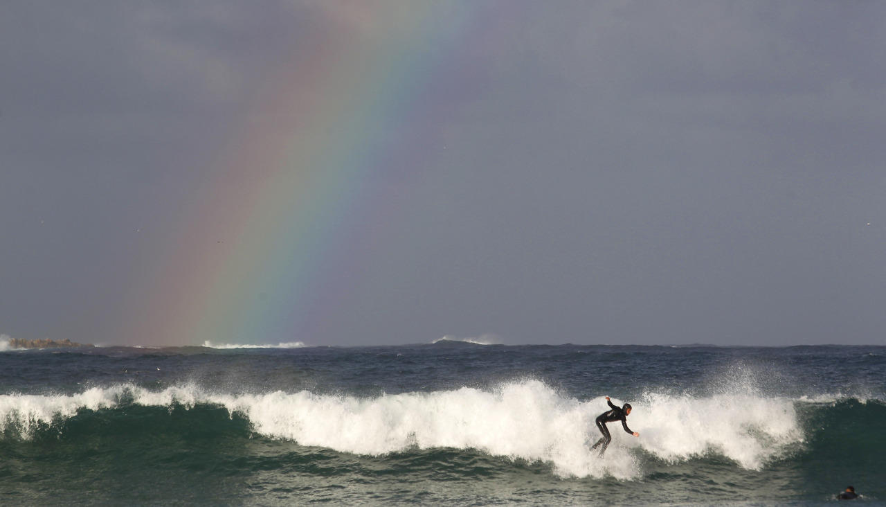 Un surfista remonta una ola en el Orzán, con un arco iris al fondo