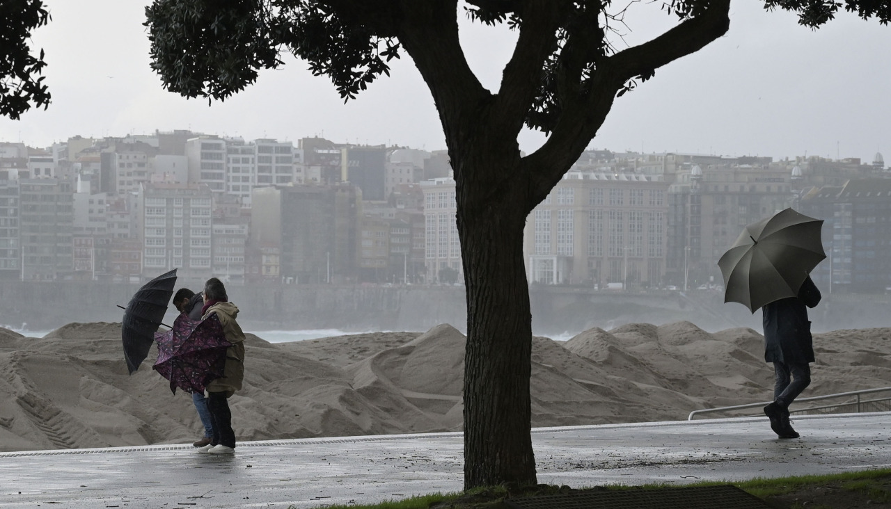 Varias personas se protegen de la lluvia junto a la costa de A Coruña