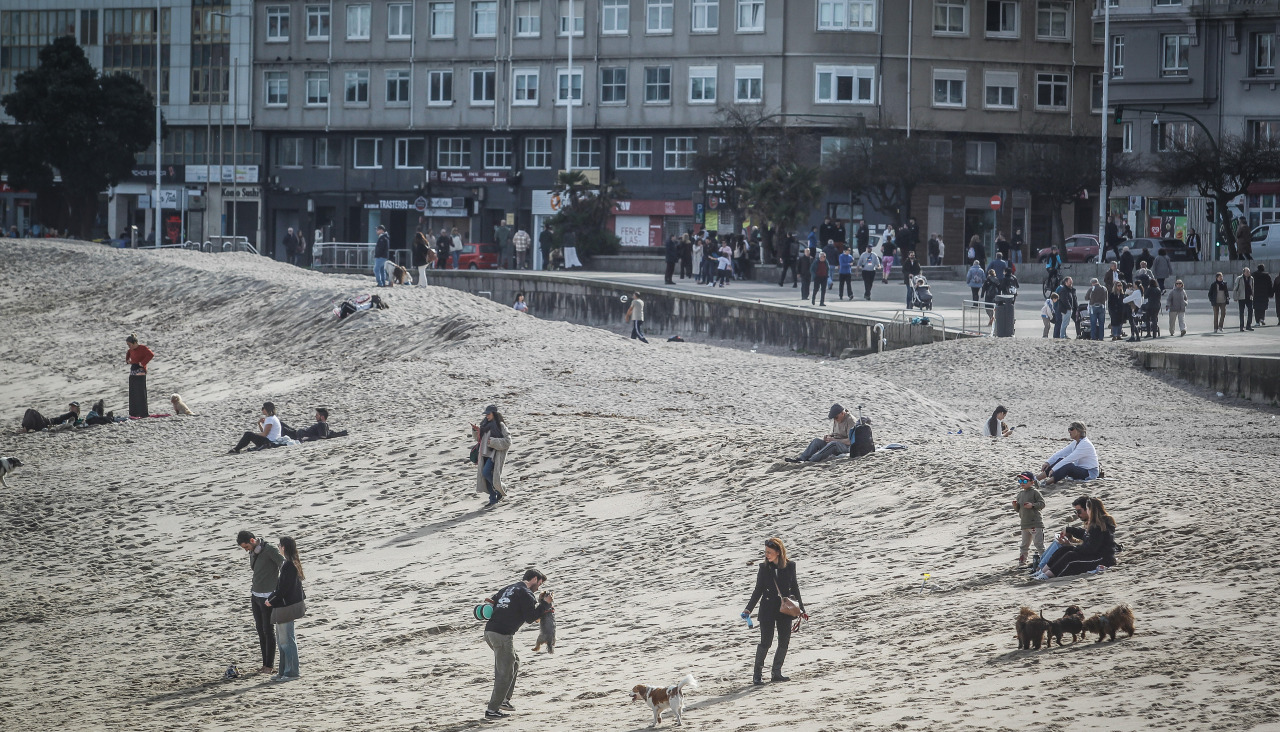 Varias personas pasean, esta mañana, por la playa de Riazor