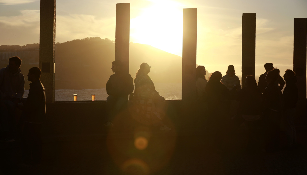 Varias personas disfrutan de unas cervezas mientras contemplan la puesta de sol la plaza de la Domus