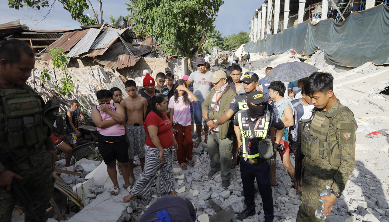 Un grupo de personas y soldados del Ejército de Filipinas contemplan un muro colapsado, un día después del terremoto