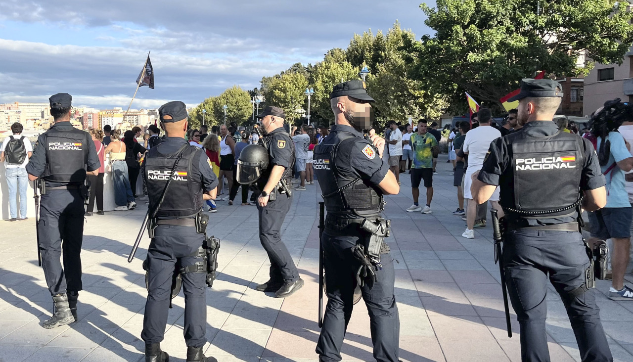 Efectivos policiales vigilan a ciudadanos que impiden el acceso a miembros de Cruz Roja para entregar alimentos a los migrantes en la playa del Trampolín, este jueves en Ceuta