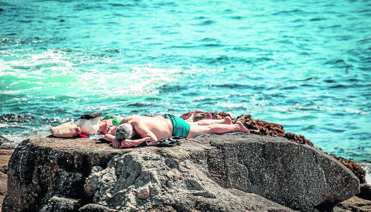 Dos personas toman el sol en unas rocas en Riazor