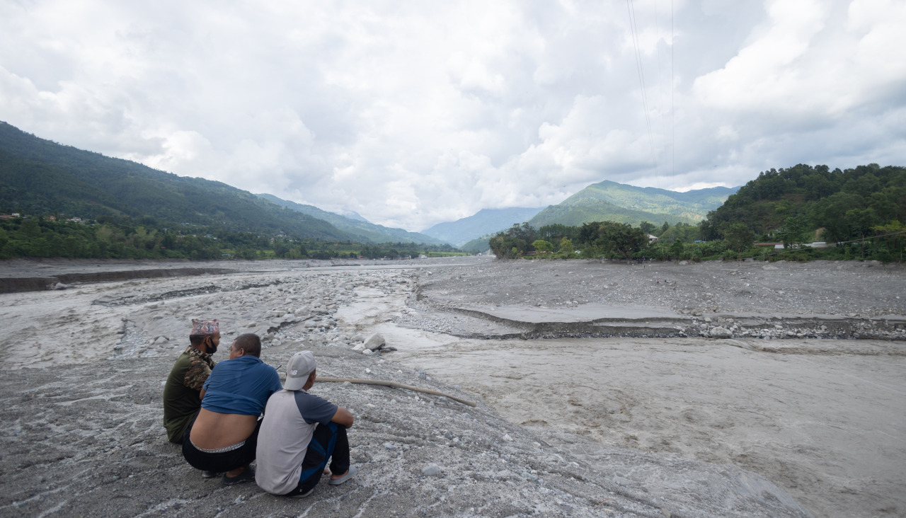 Tres hombres observan cómo el agua fluye por una comunidad afectada por una inundación glacial cerca de la frontera entre Nepal y China que mató a cientos de personas